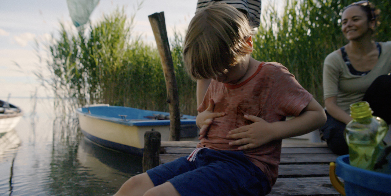 Lille dreng sad ved en sø og blev snavset på sin t-shirt